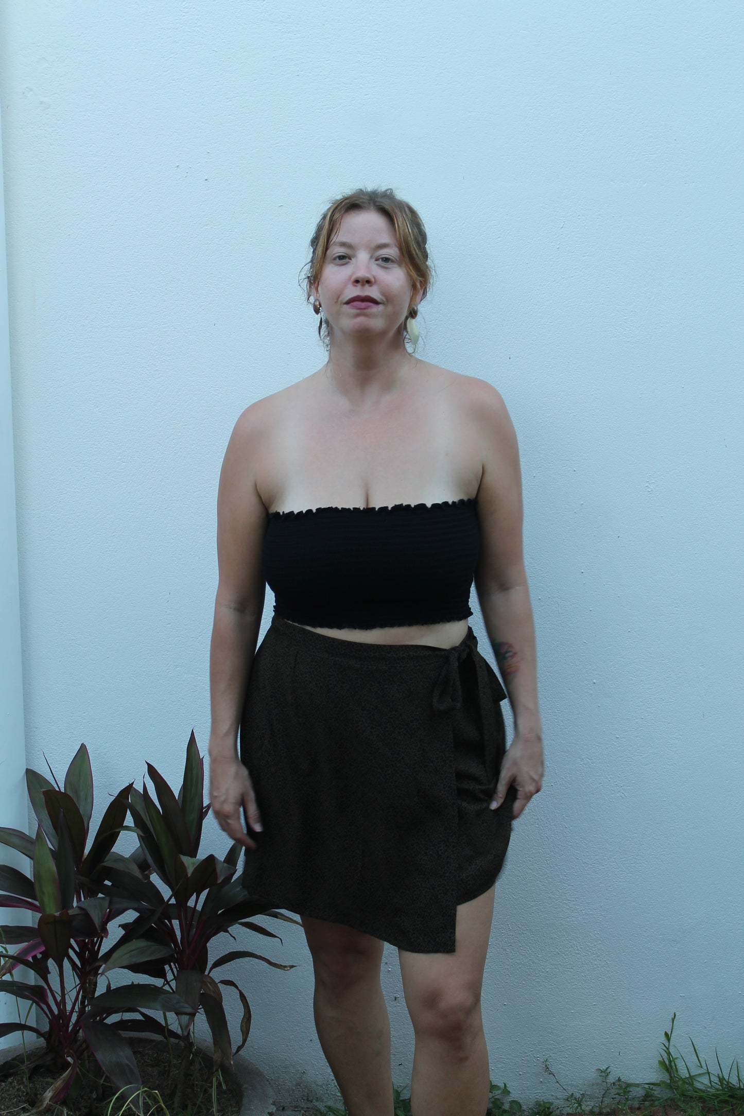 Person wearing a black and white dress standing against a light blue wall with plants.