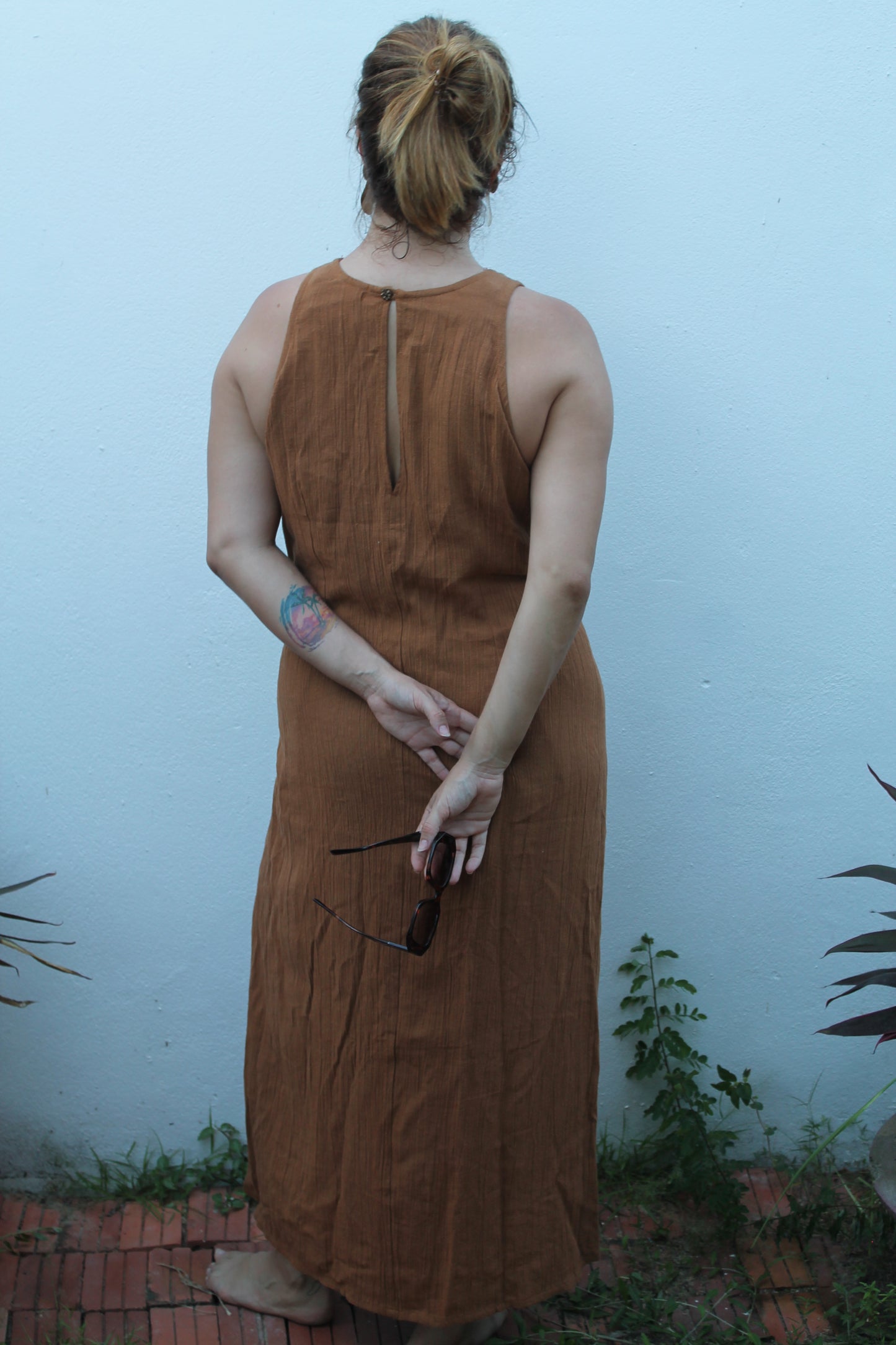 Person wearing a brown dress against a light blue wall with plants.