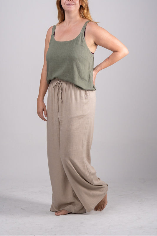 Woman wearing a green tank top and beige wide-leg pants on a gray background