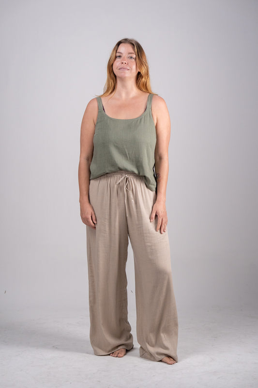 Woman wearing a green tank top and beige pants on a plain background