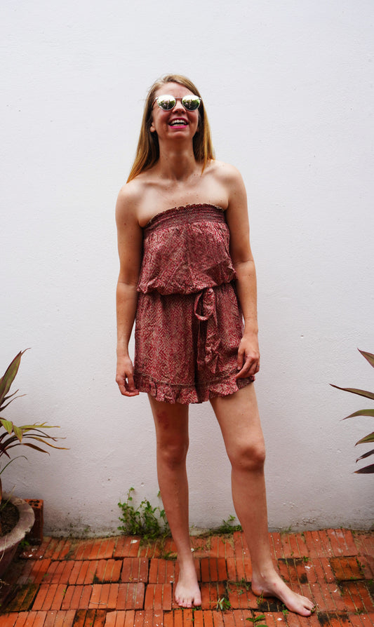 Woman wearing a strapless floral dress standing against a white wall with plants around.