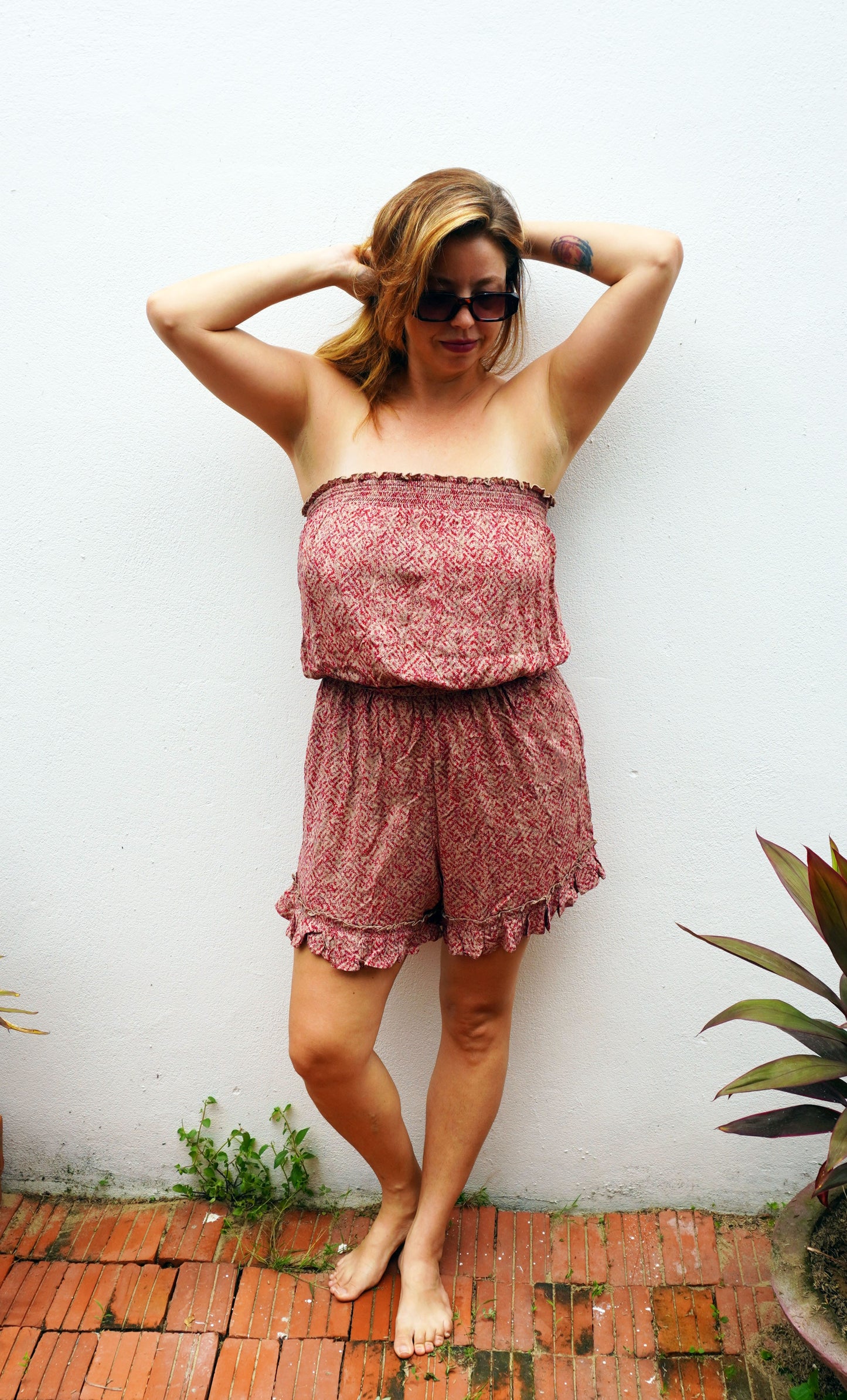 Woman wearing a strapless floral romper against a white wall.