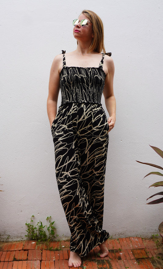 Woman wearing a black and cream patterned jumpsuit against a white wall.