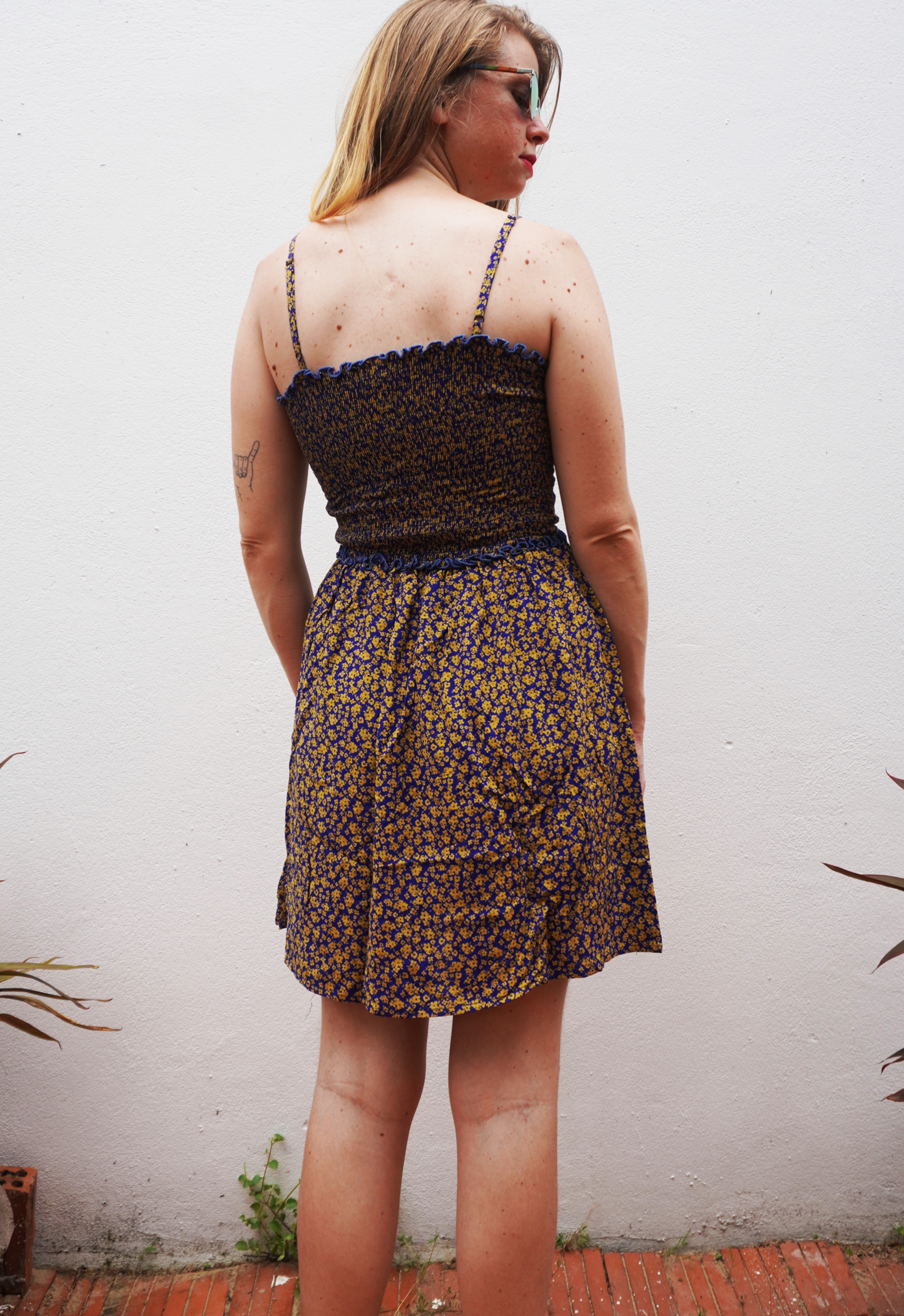 Woman wearing a purple and yellow floral dress against a white wall.