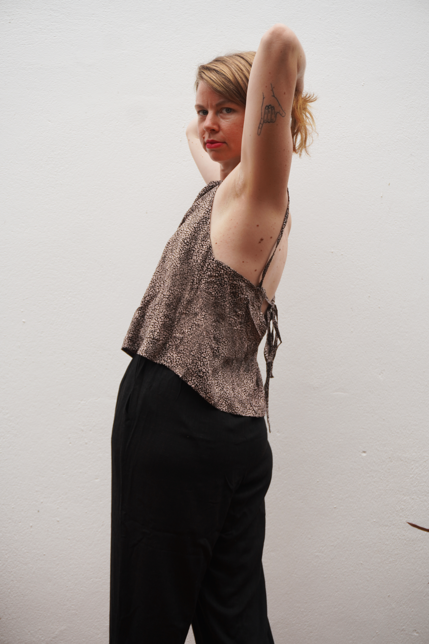 Woman wearing a patterned top and black pants against a plain background