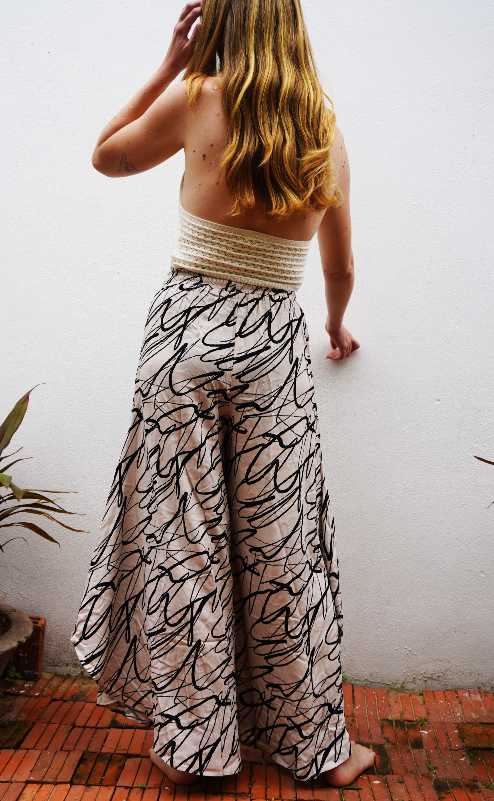 Person wearing a white top and patterned pants against a white wall.