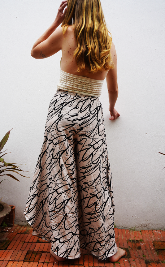 Person wearing a white top and patterned pants against a white wall.