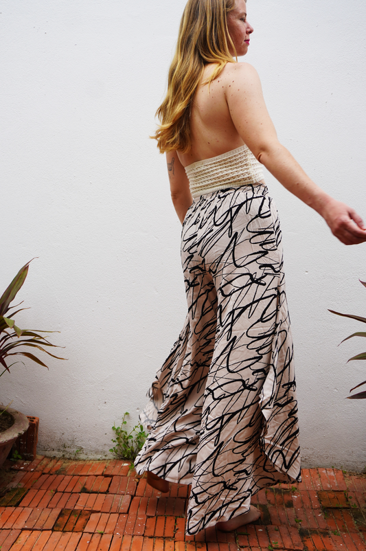 Woman wearing a strapless top and patterned pants standing against a white wall.