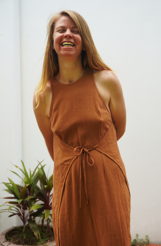 Woman wearing a brown dress standing indoors with a plant in the background