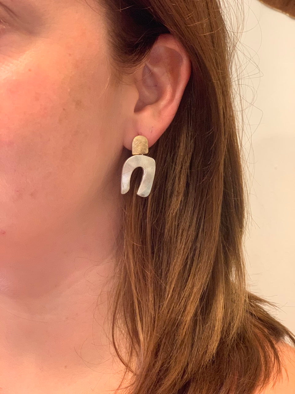 woman wearing silver horseshoe with gold detail earrings.