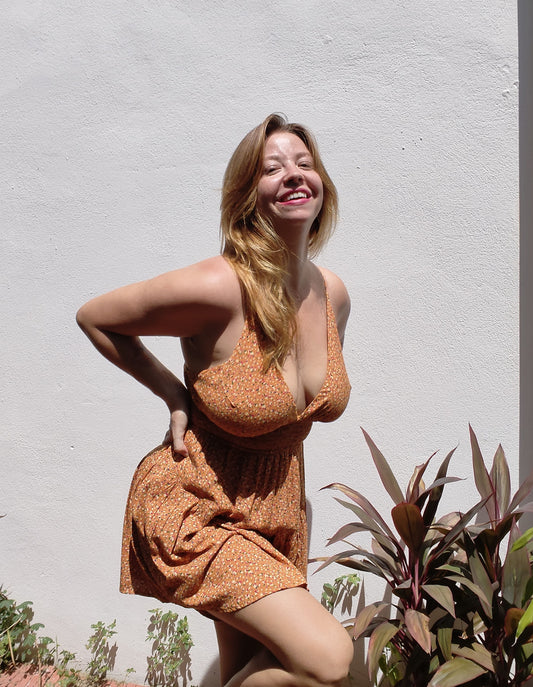 Woman in a patterned dress standing against a light gray wall with plants around.