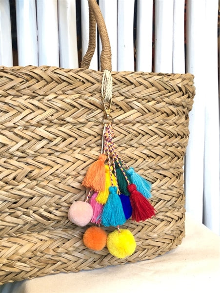 Colorful pom pom tassels on a straw bag.