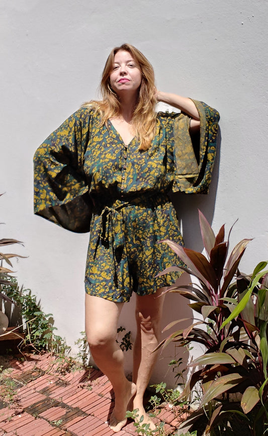 Woman wearing a peackock patterned outfit standing outdoors with plants around.