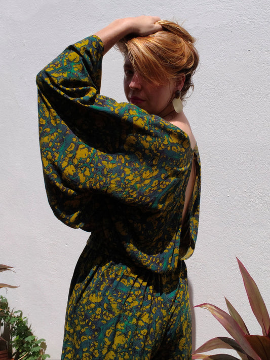 Person wearing a green and yellow patterned outfit against a white wall with plants.