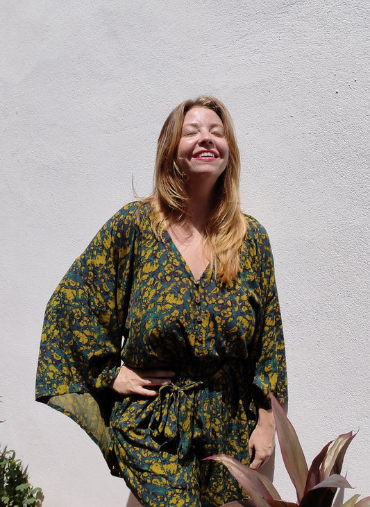 Woman wearing a green and yellow patterned one-piece against a light gray wall.