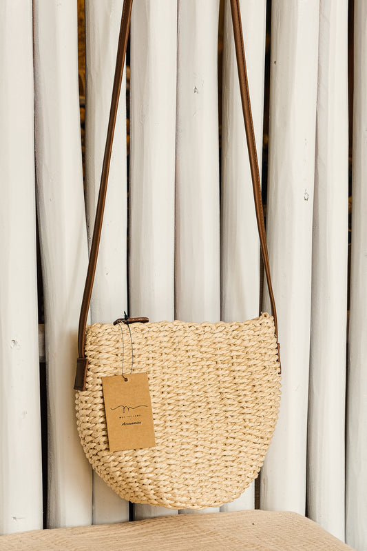 Woven handbag with a tag on a wooden surface against a white curtain background