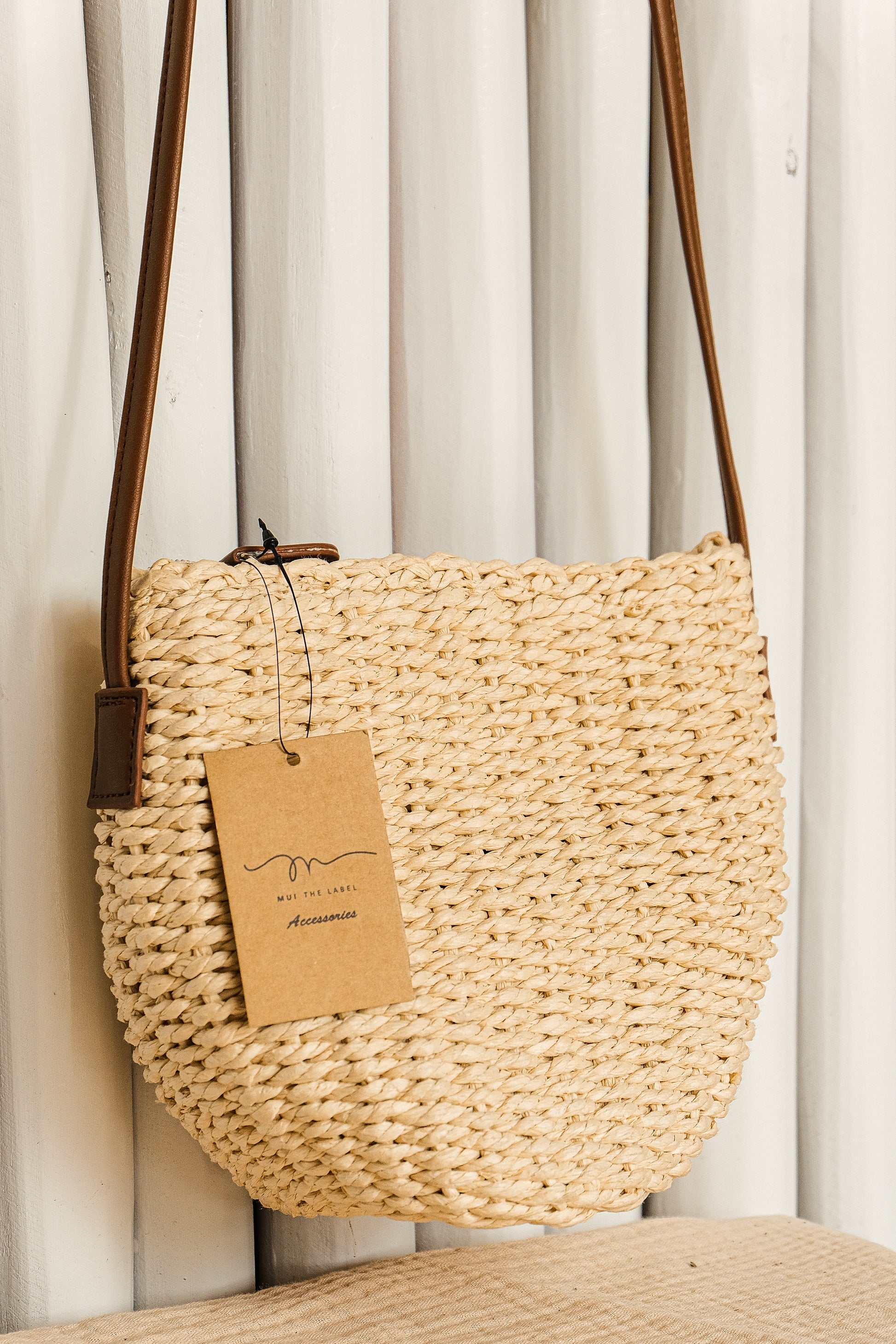 Woven handbag with a tag against a neutral background