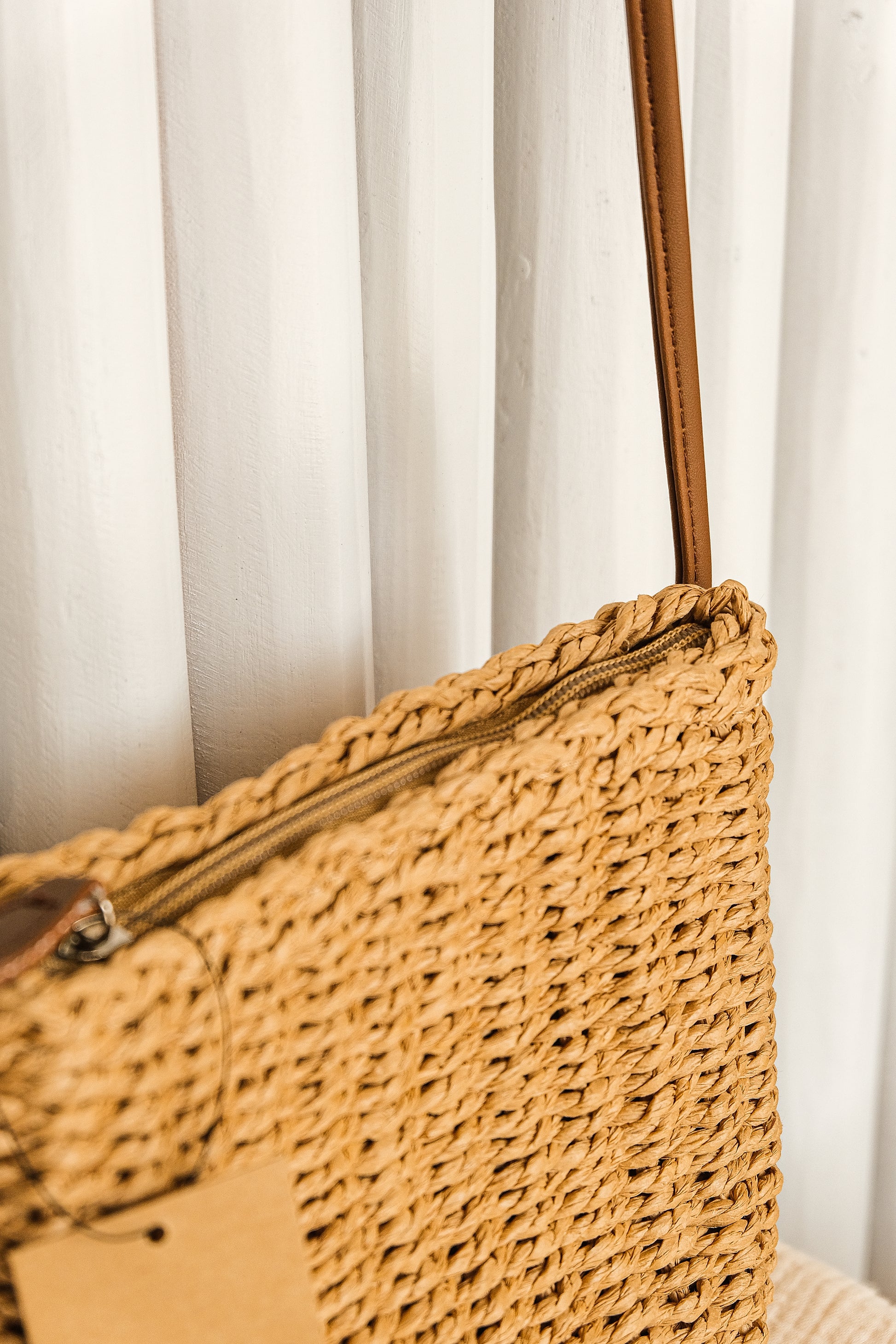 Close-up of a woven handbag with a brown handle against a white curtain background