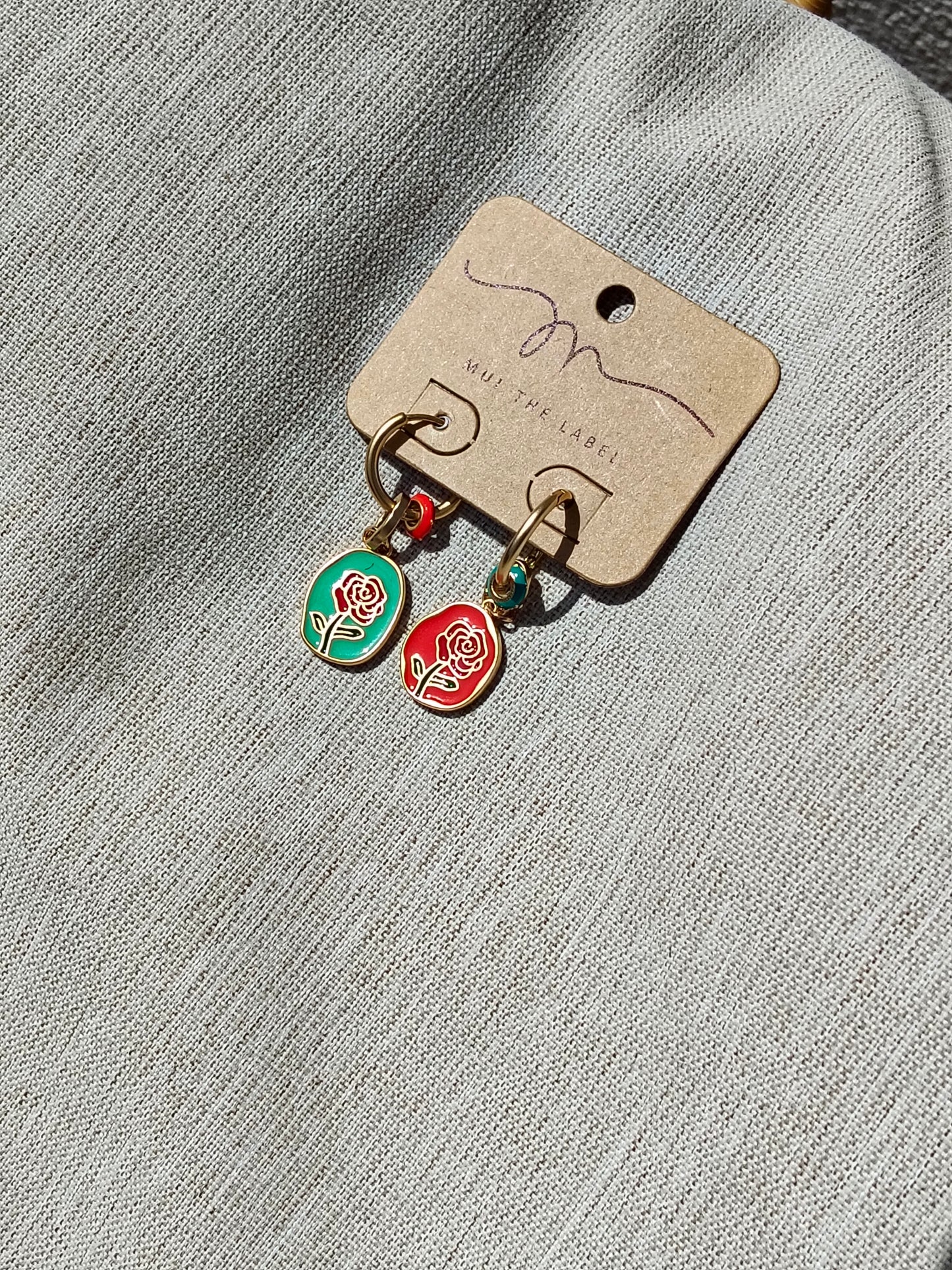 Pair of earrings with rose charms on a branded card against a textured gray background