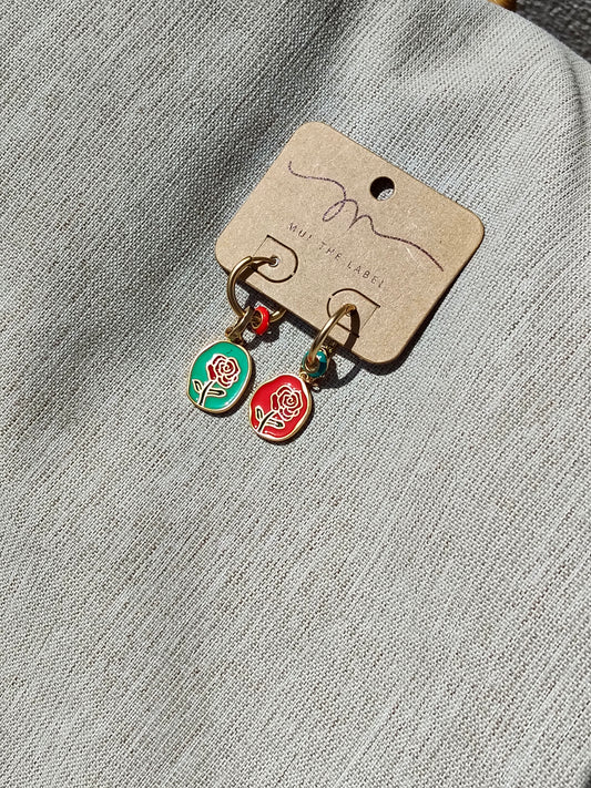 Pair of earrings with rose charms on a branded card against a textured gray background