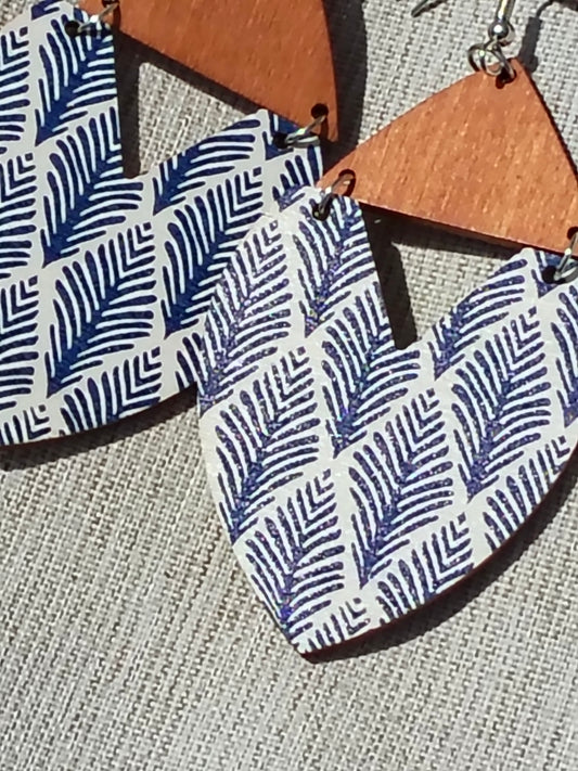 Wooden earrings with blue leaf pattern on a textured surface