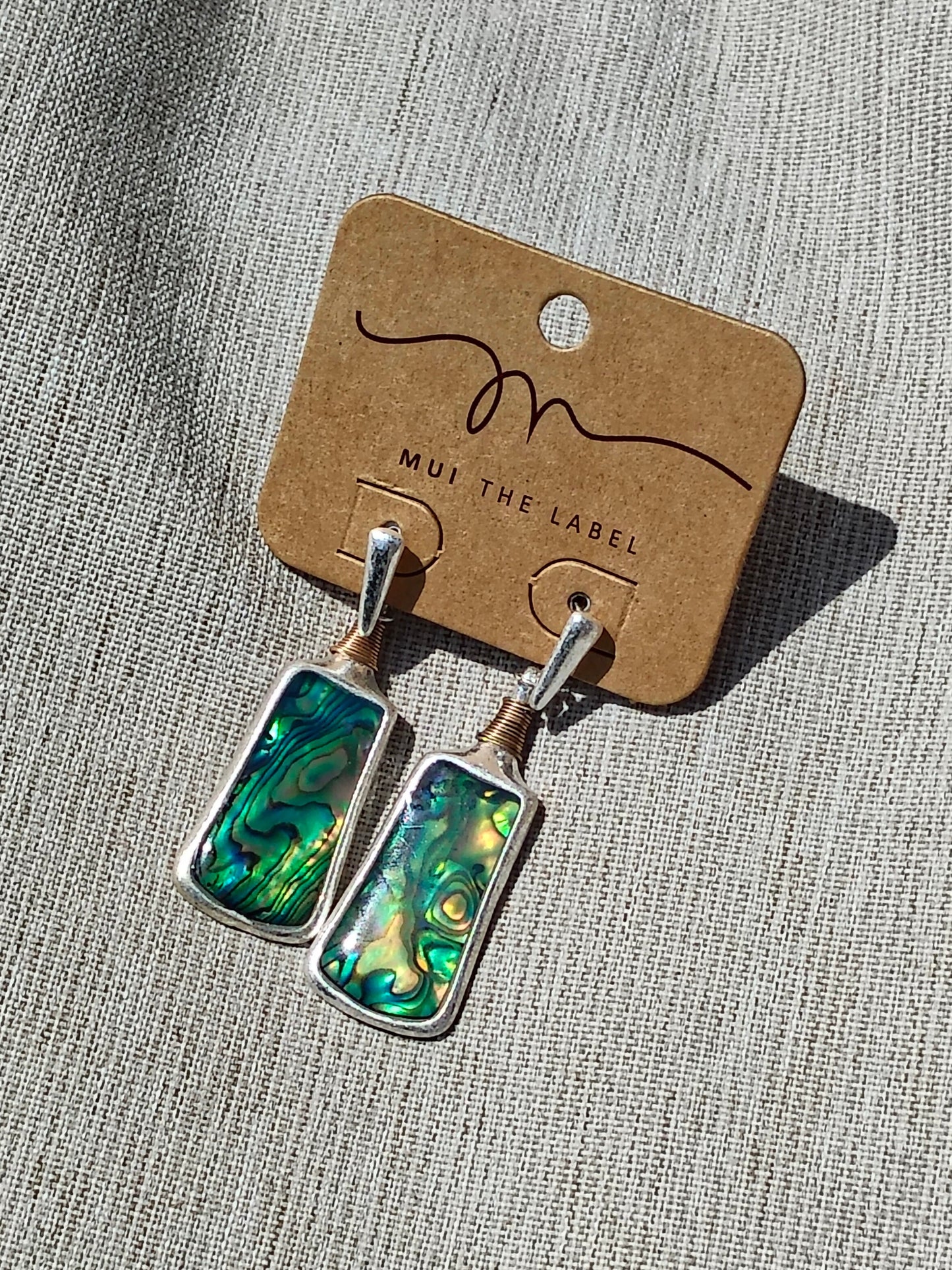 Pair of Mother of Pearl earrings on a 'Mui The Label' card against a textured gray background