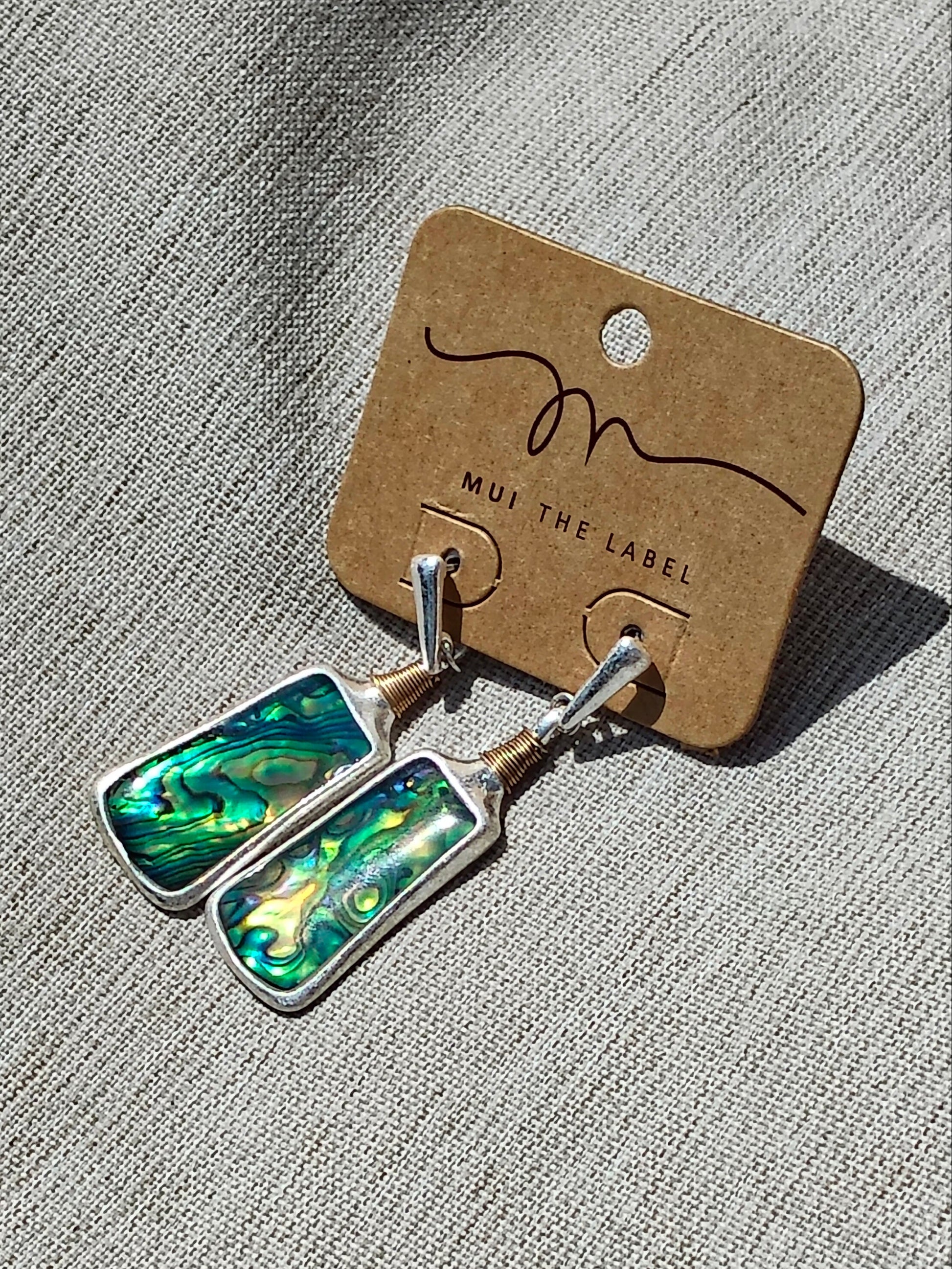 Pair of Mother of Pearl earrings on a 'Mui The Label' card against a textured gray background