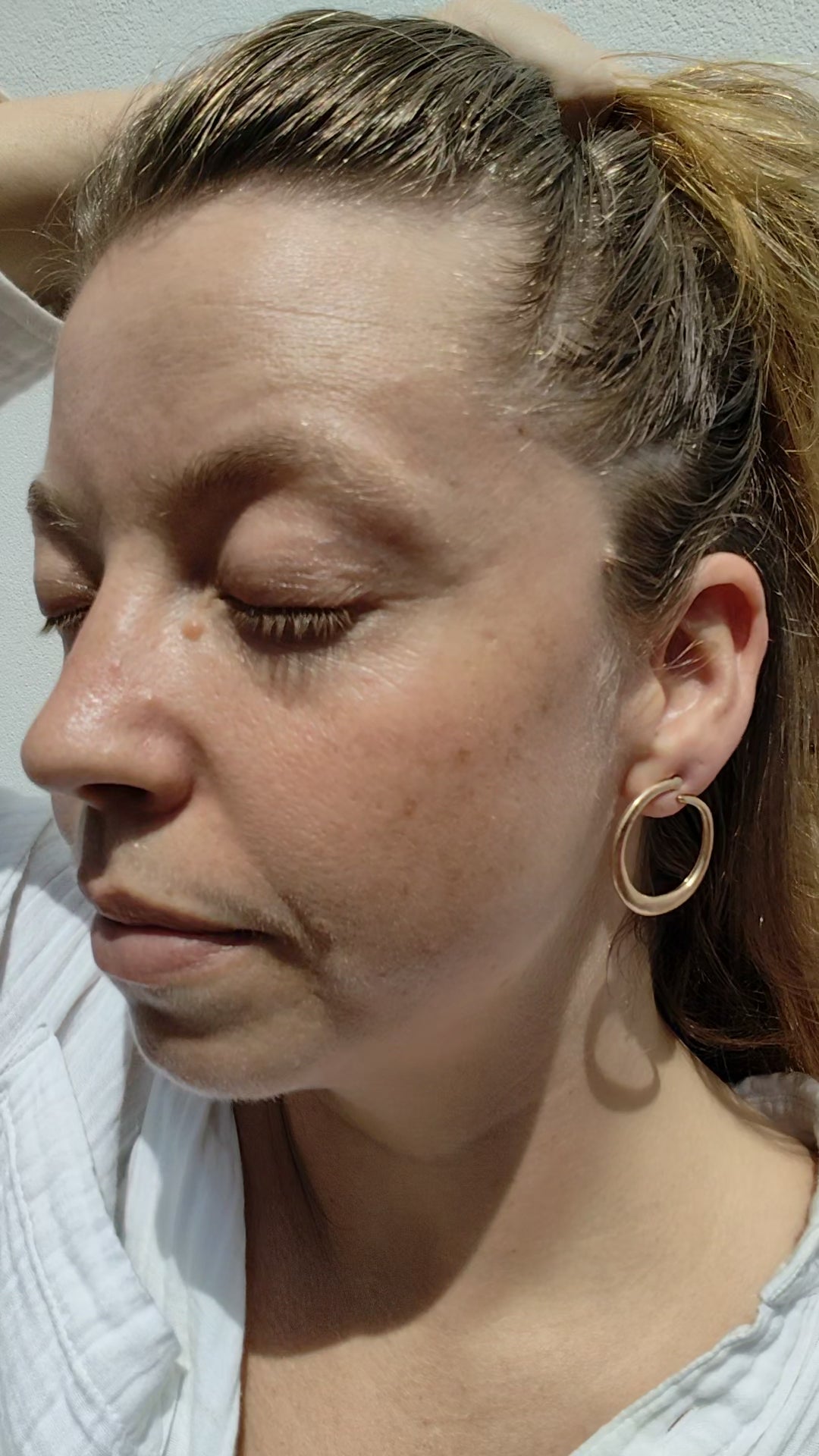 Close-up of a woman with a gold hoop earring against a neutral background