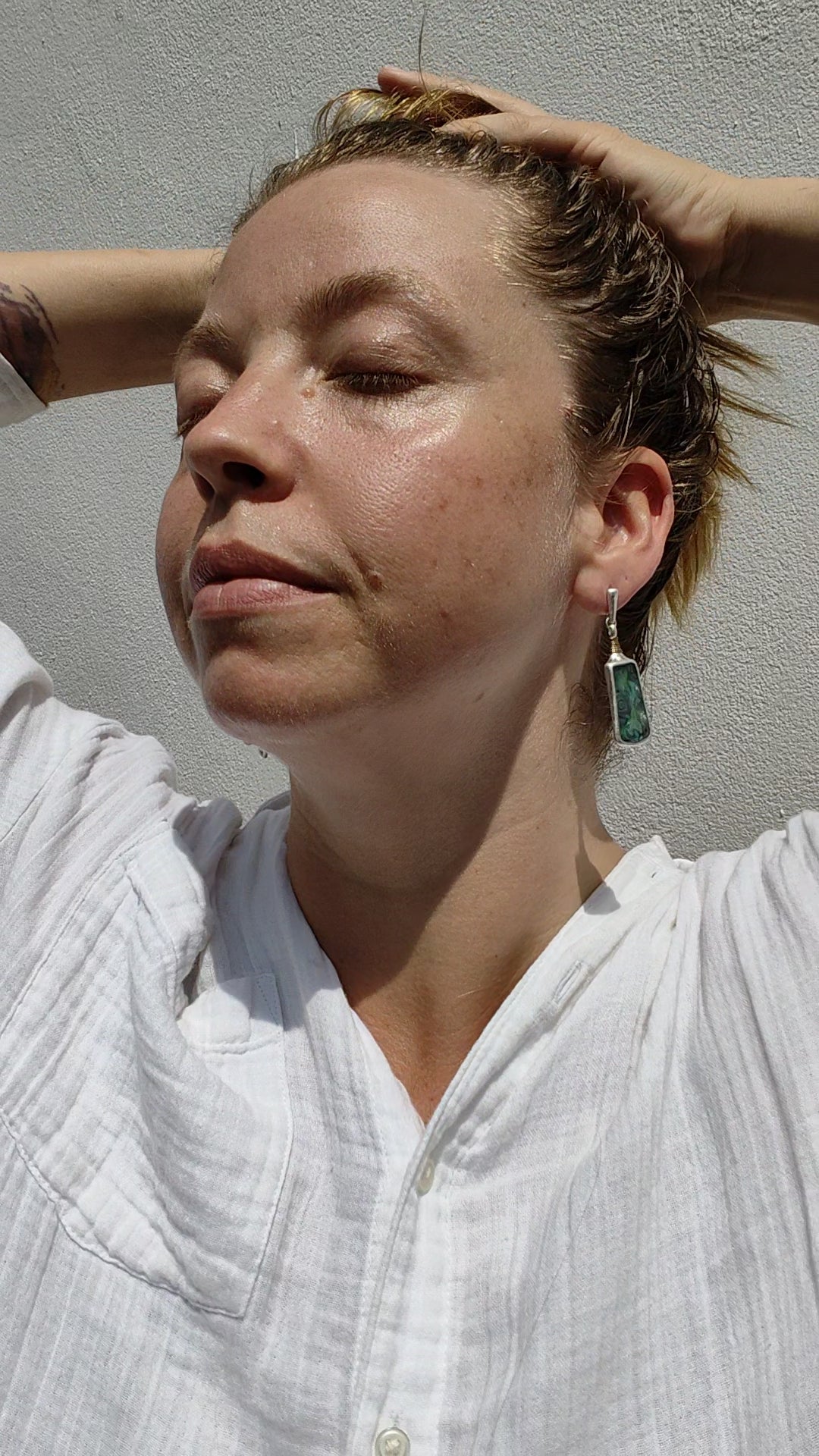 Close-up of a person wearing a pair of Mother of Pearl earrings with a neutral background
