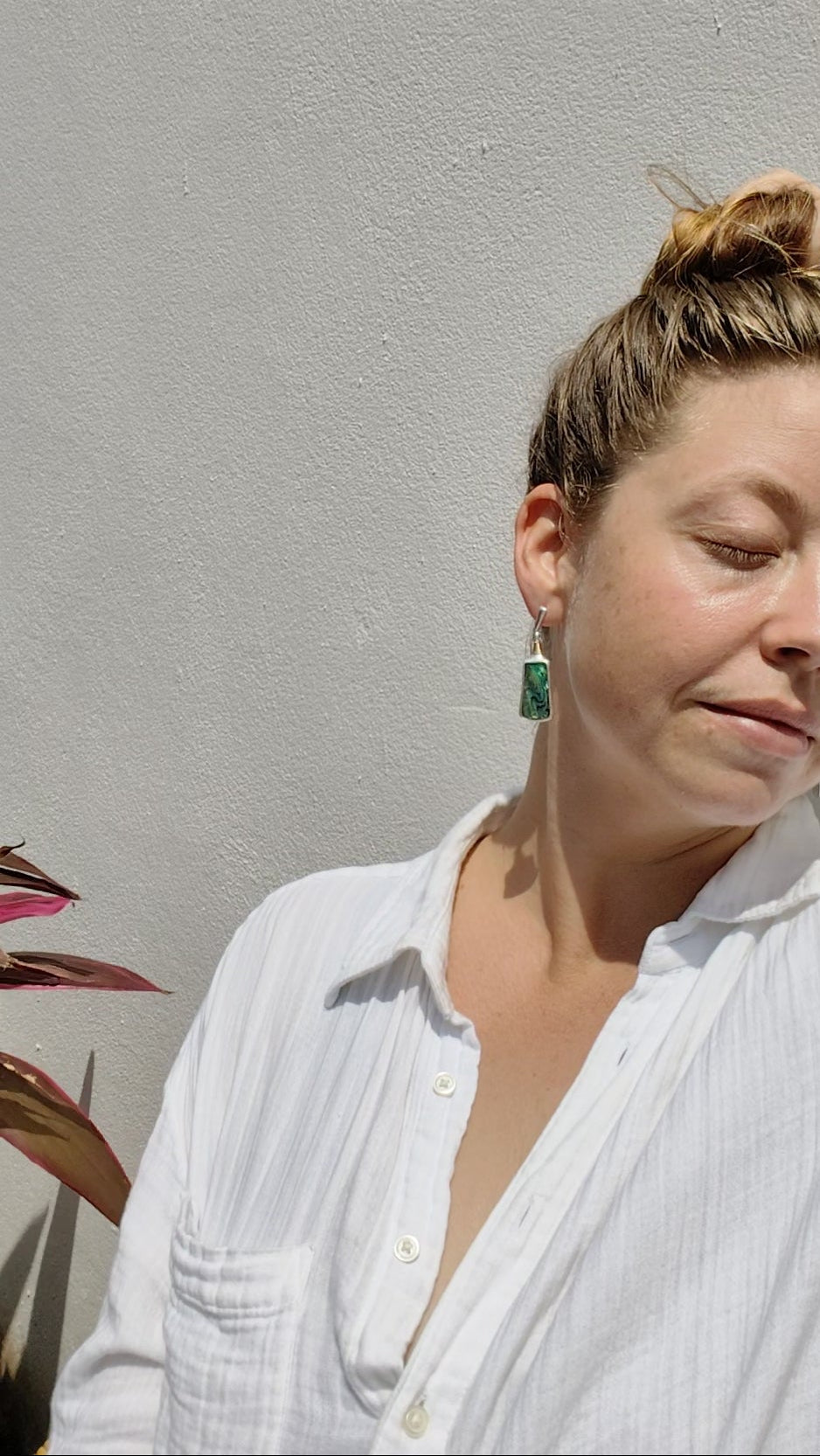 Close-up of a person wearing a pair of Mother of Pearl earrings with a neutral background