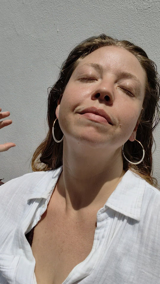 Woman with closed eyes against a plain background wearing large hoop earrings.