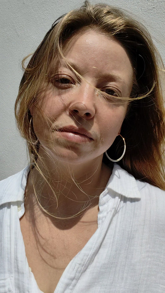 Woman wearing a white shirt against a plain background, wearing large hoop earrings. 