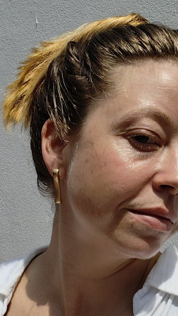 Woman wearing gold earrings and a white shirt against a gray background