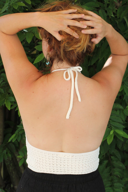 Person wearing a white bikini top with a black cover-up in a green outdoor setting