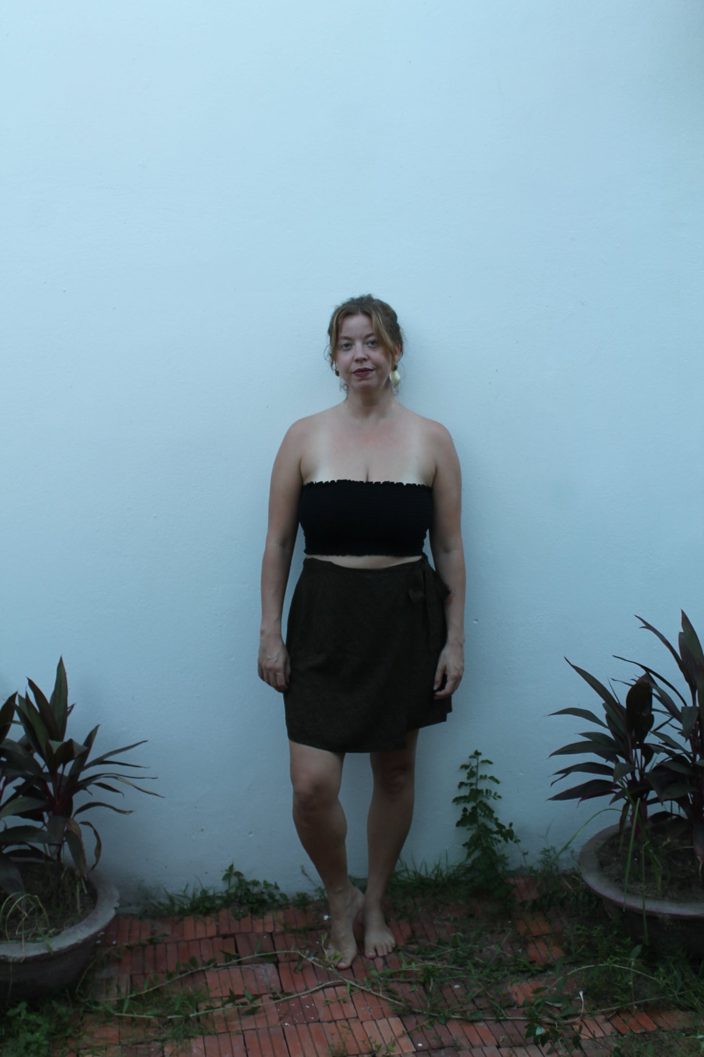 Person wearing a black dress standing against a light blue wall with plants around.