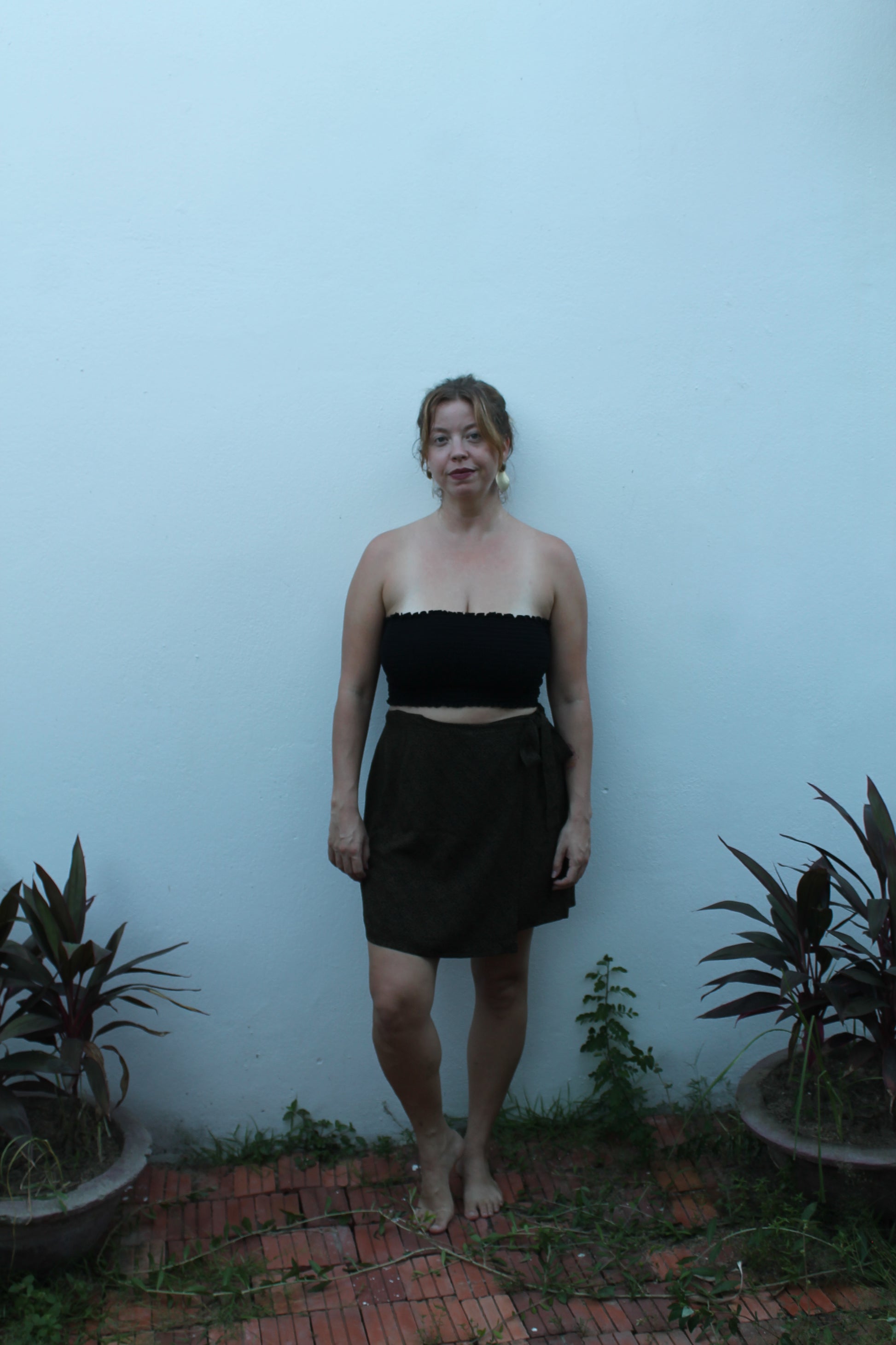 Person wearing a black dress standing against a light blue wall with plants around.