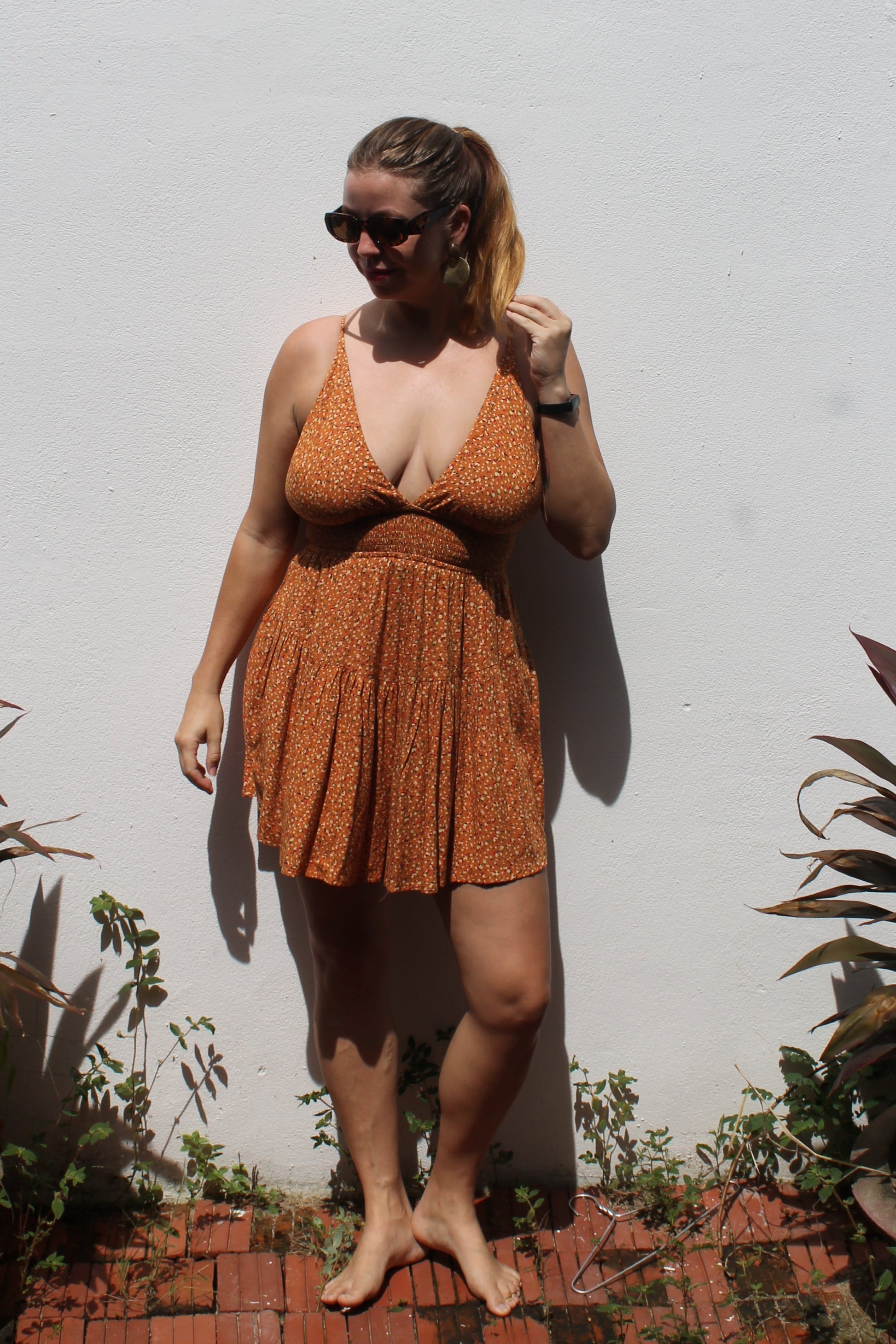 Person wearing a brown playsuit standing on a white surface with plants around
