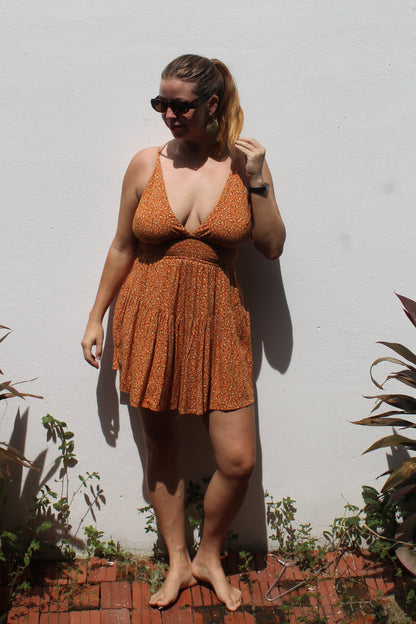 Person wearing a brown playsuit standing on a white surface with plants around