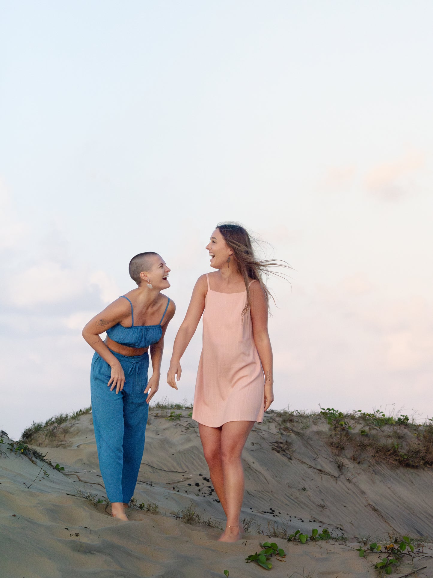 Two women walking on a sandy dune with a clear sky.