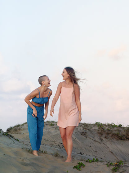 Two women walking on a sandy dune with a clear sky.