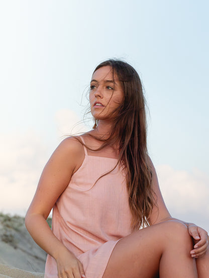Woman in a pink dress sitting on a beach with a clear sky.