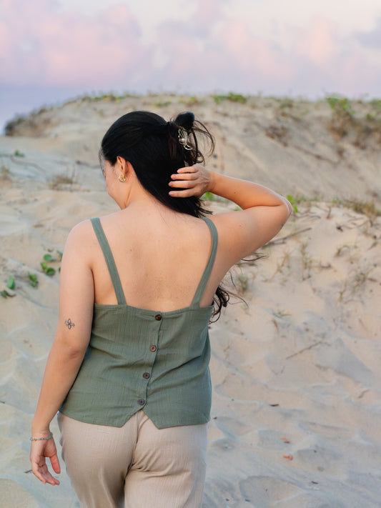 A woman on a beach wearing a dark grey top with buttons.