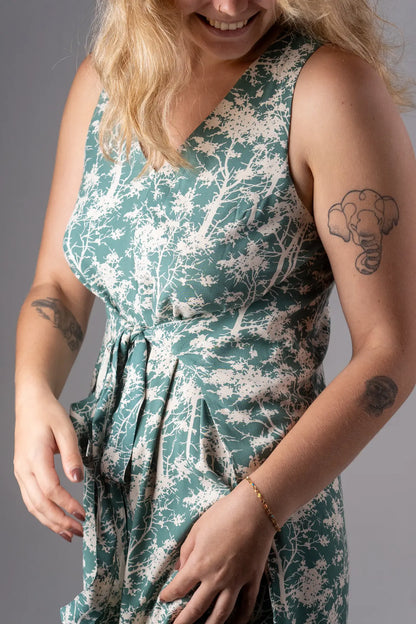 Woman wearing a green floral dress with tattoos on her arms against a gray background