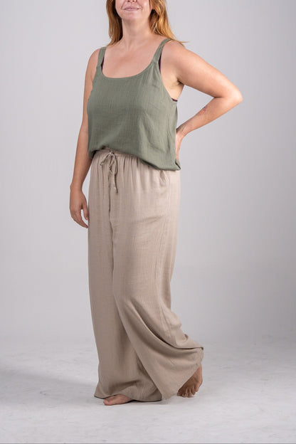 Woman wearing a green tank top and beige wide-leg pants on a gray background