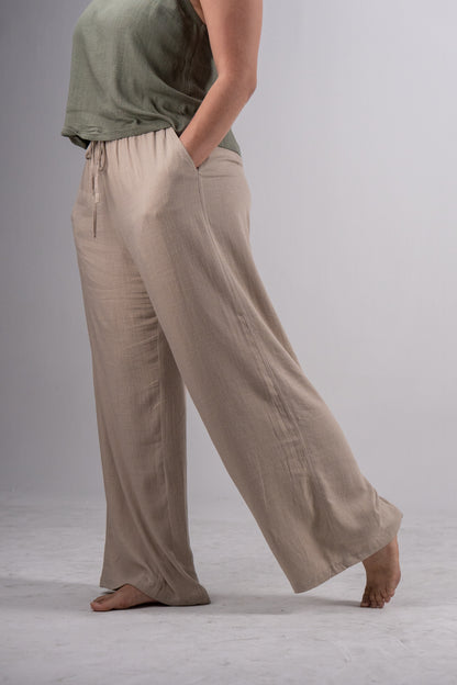Person wearing beige wide-leg pants and a green top on a plain background