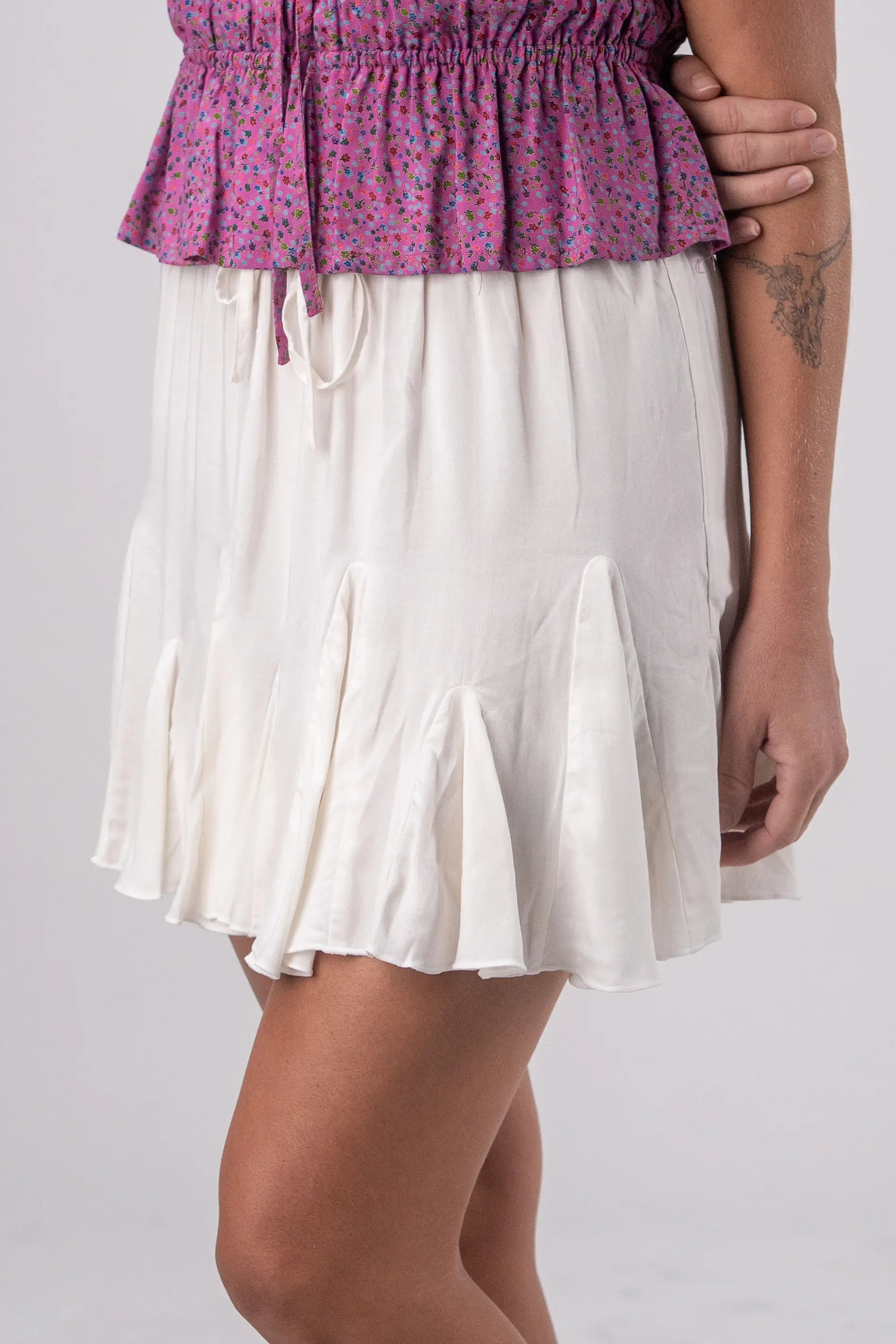 Person wearing a pink floral top and white skirt on a plain background