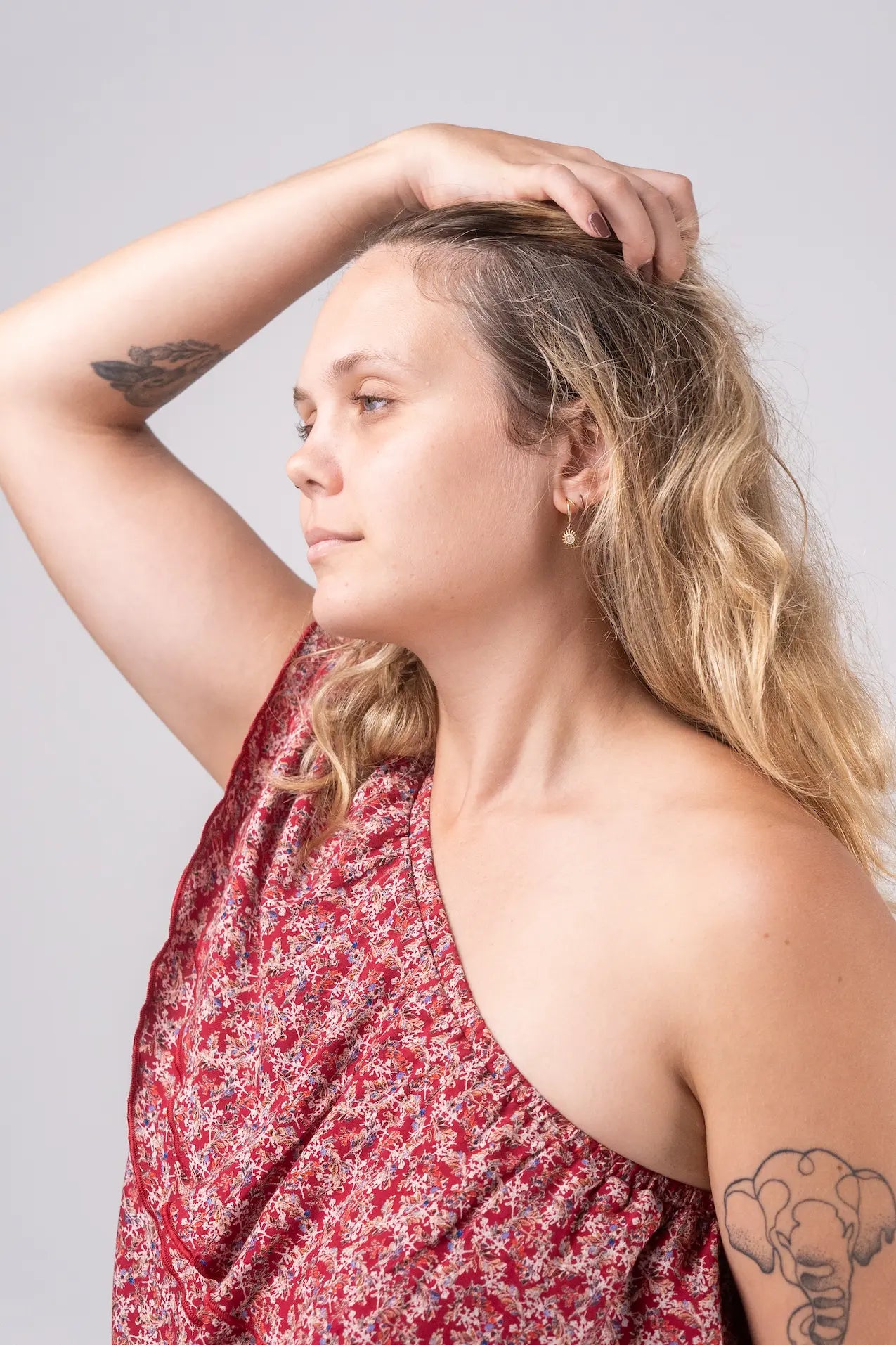 Woman with tattoos wearing a red floral dress against a plain background