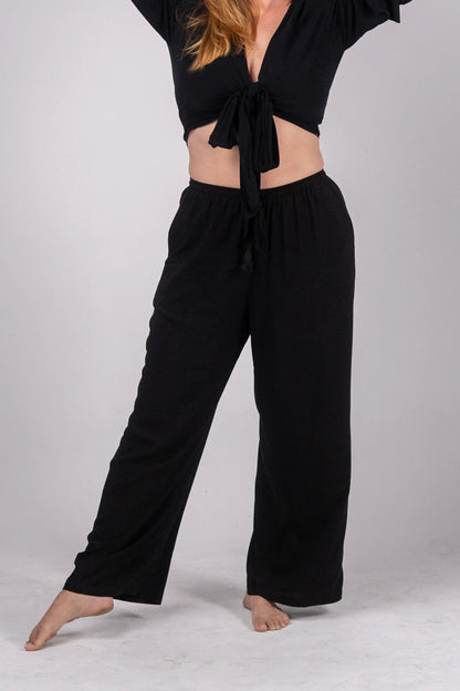 Woman wearing a black outfit with a tied top and wide-leg pants on a plain background
