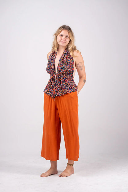 Woman wearing a patterned top and orange pants on a white background
