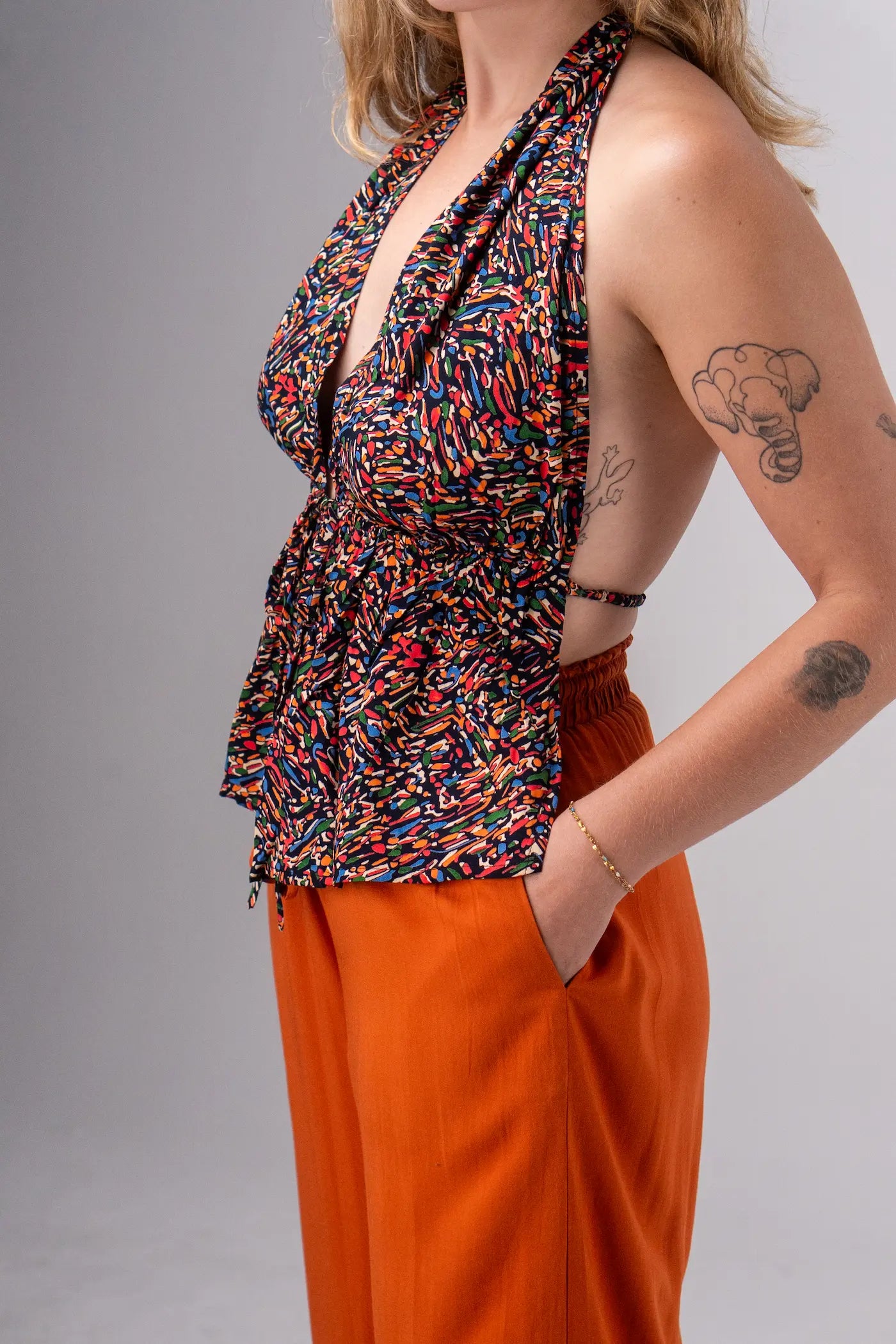 Woman wearing a colorful top and orange pants against a gray background